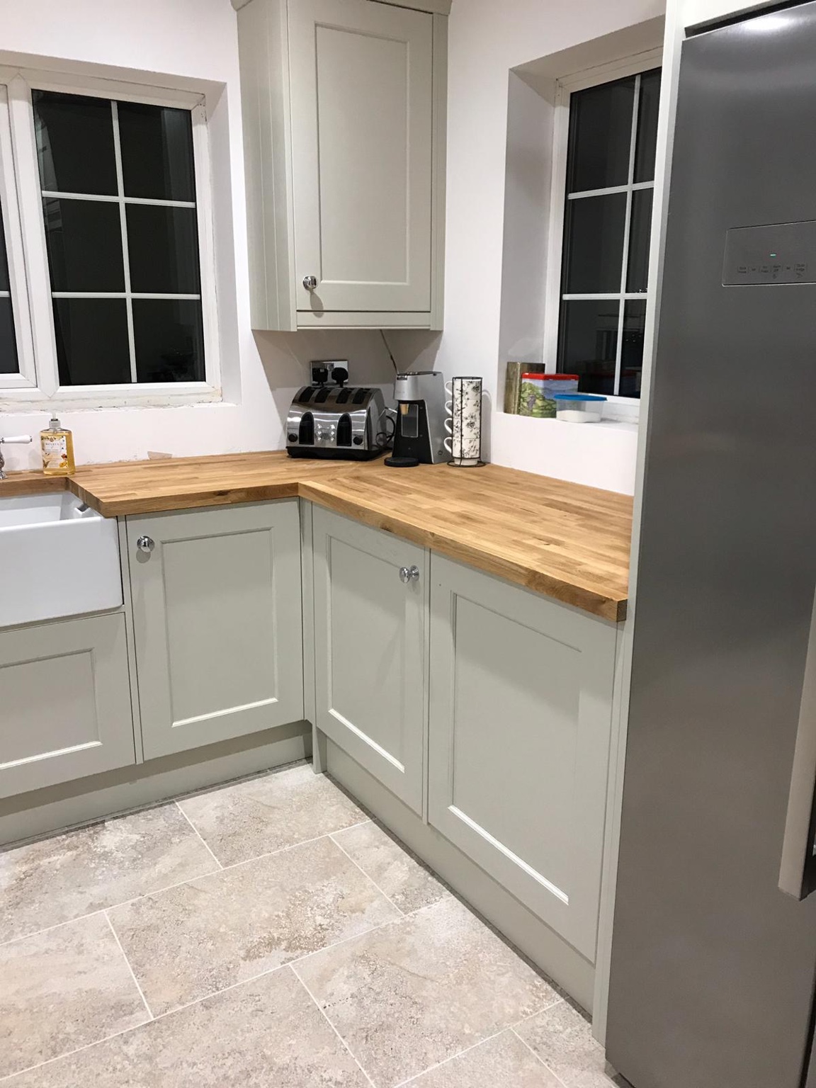 Corner of light grey kitchen cabinetry with oak worktop